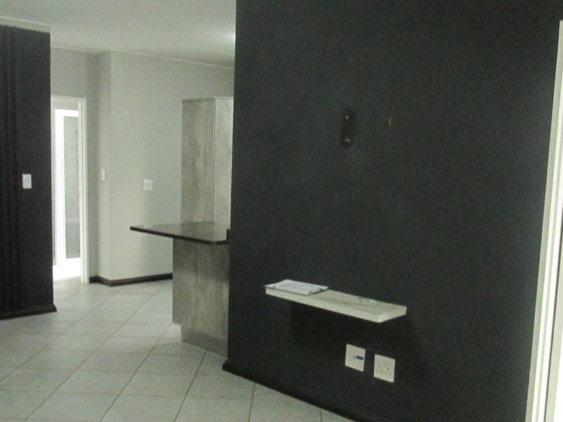 An open-plan living area featuring tiled flooring, a built-in breakfast bar, and a dark accent wall with a mounted shelf.