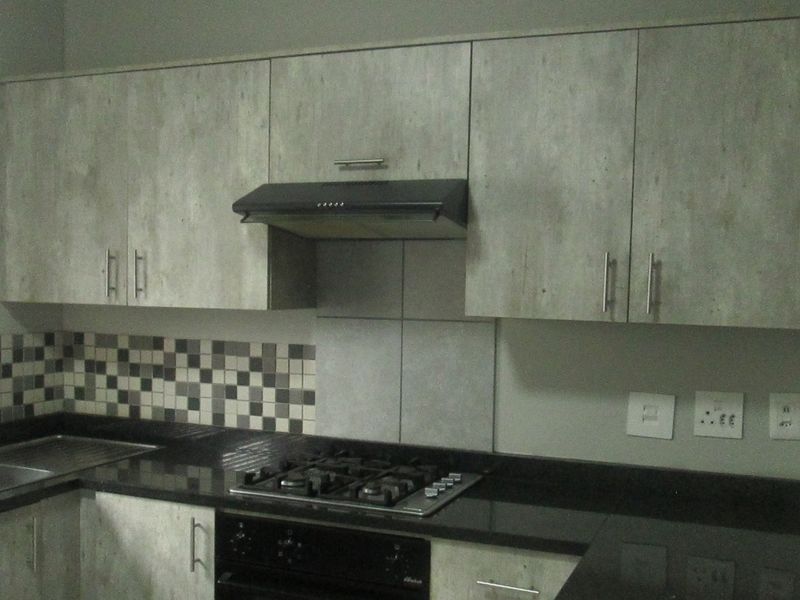 A functional kitchen featuring modern grey-toned cabinetry, granite countertops, a gas hob with extractor fan, and a tiled backsplash.