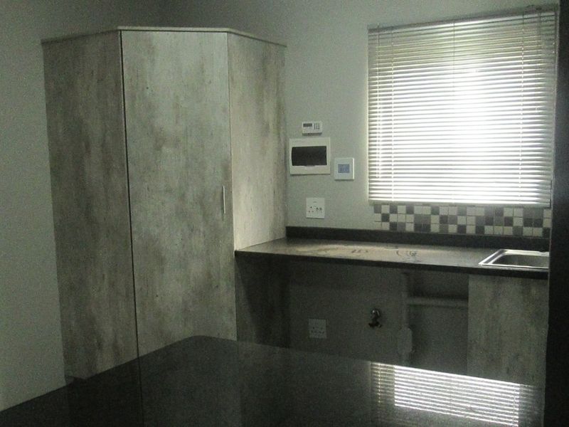 A functional scullery area featuring built-in cabinetry, a stainless steel sink, laminate countertops, and a tiled splashback with venetian blinds.