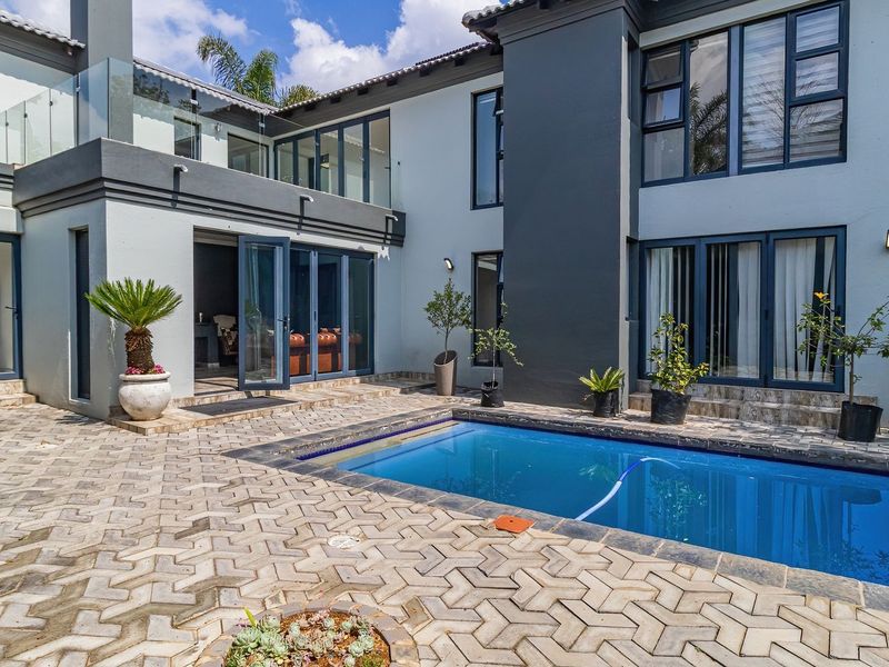 A well-maintained rear courtyard featuring a swimming pool, paved patio area, and modern architectural details including glass balustrades and bi-fold doors.