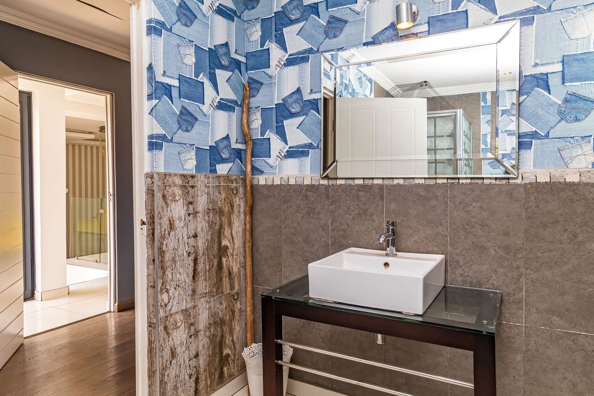A bathroom featuring a modern vessel sink, chrome faucet, and a decorative mirror, set against a unique denim-patterned wallpaper and tiled wall finish.
