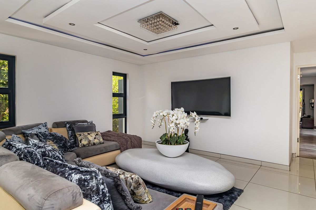 Modern living room featuring tiled flooring, a recessed ceiling with downlights, and large aluminium-framed windows providing natural light.