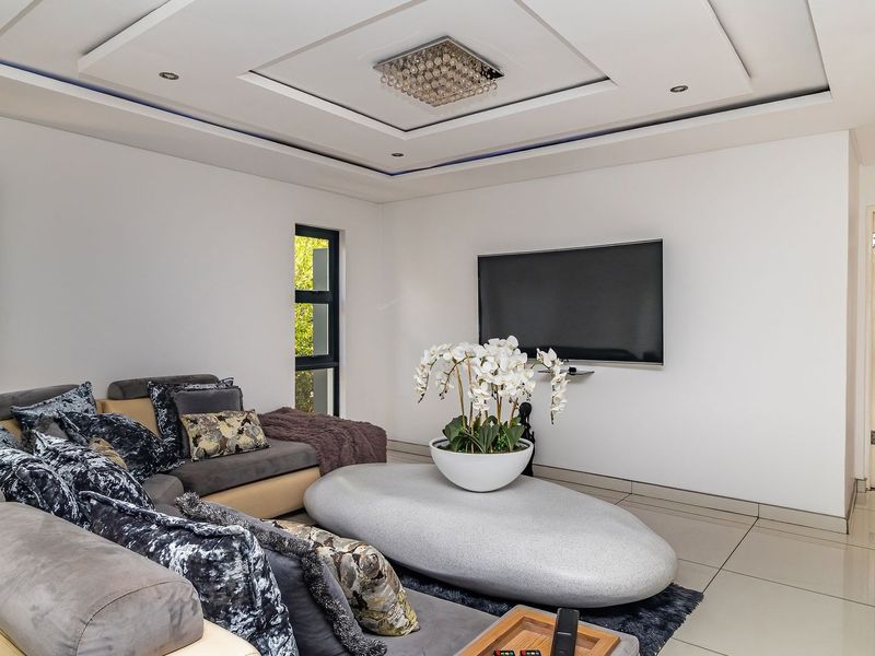 Modern living room featuring tiled flooring, a recessed ceiling with downlights, and large aluminium-framed windows providing natural light.