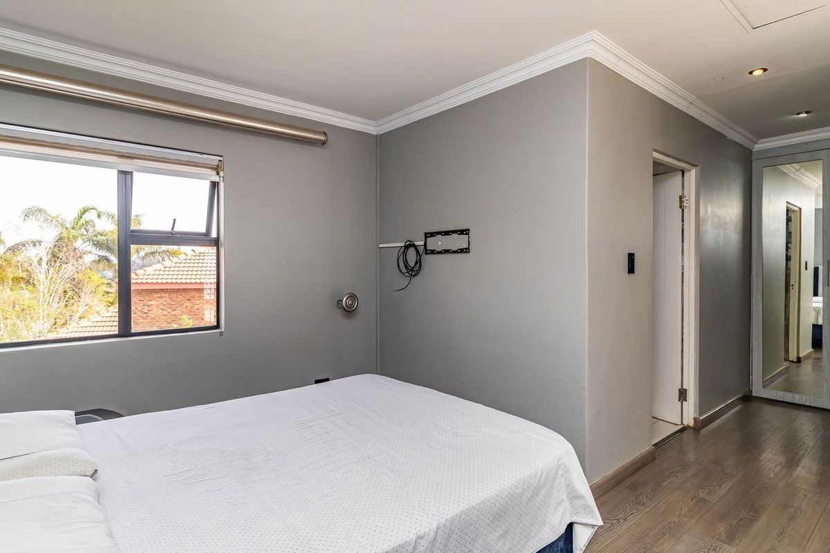 A bedroom featuring laminate flooring, built-in cupboards with mirrored doors, recessed lighting, and a window with an exterior view.