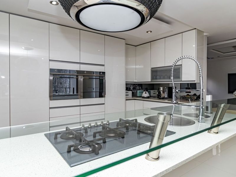 Modern kitchen featuring high-gloss cabinetry, quartz countertops, a central island with a gas hob, and integrated built-in ovens.