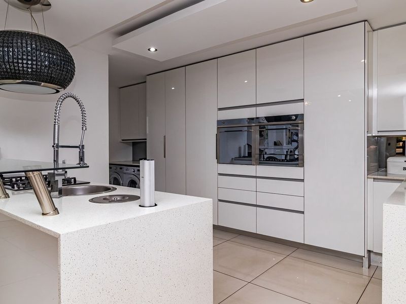 Modern kitchen featuring high-gloss cabinetry, quartz countertops, integrated double ovens, and a central island with a gas hob and prep sink.