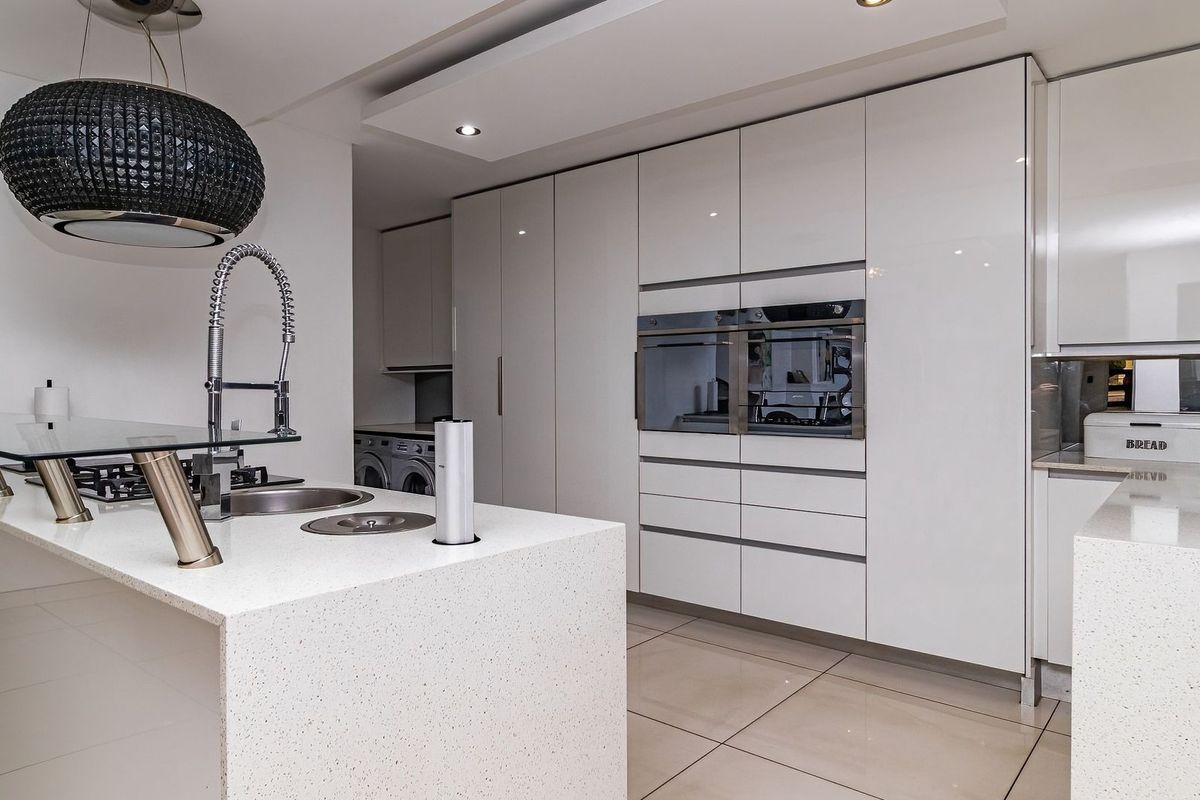 Modern kitchen featuring high-gloss cabinetry, quartz countertops, integrated double ovens, and a central island with a gas hob and prep sink.