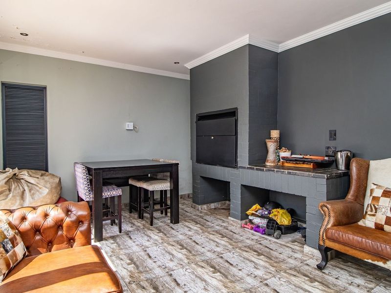 Covered patio area featuring a built-in braai, tiled flooring, and direct access to the garden through a sliding door.
