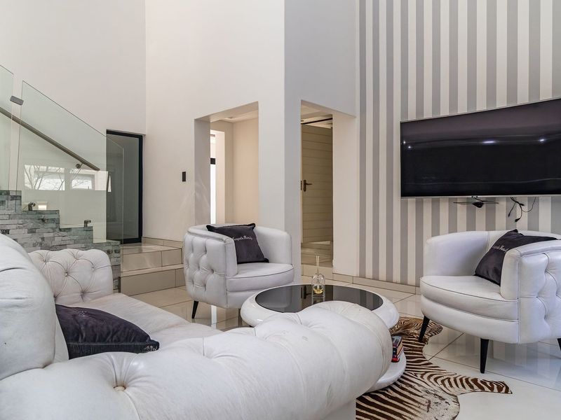 Modern living room featuring high ceilings, a striking stone-clad staircase with a glass balustrade, and polished tiled flooring.