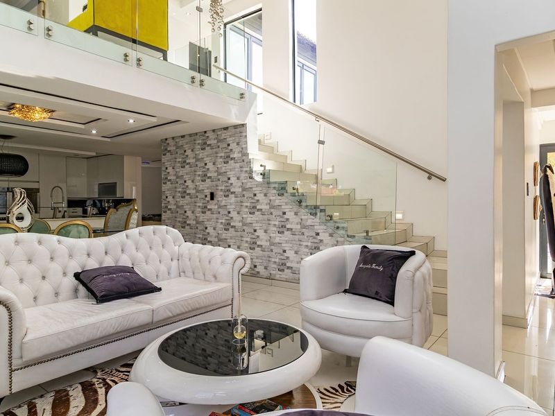 Spacious open-plan living area featuring a modern staircase with glass balustrade, stone feature wall, and integrated kitchen finishes.