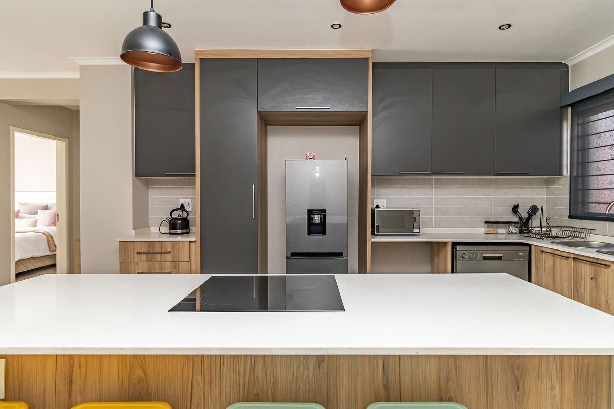 Modern kitchen featuring a central island with an integrated induction cooktop, sleek dark grey and wood-tone cabinetry, stone countertops, and contemporary pendant lighting.