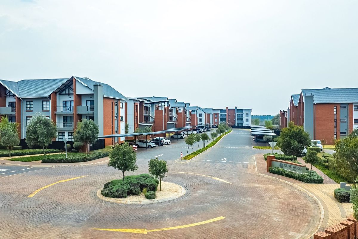 Aerial view of a modern townhouse complex featuring paved driveways, covered parking bays, and well-maintained landscaped grounds.