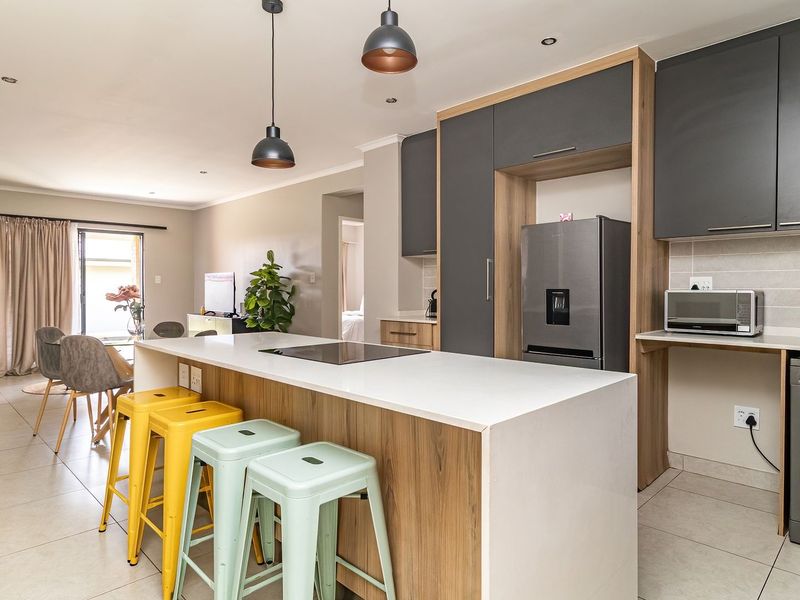 Modern open-plan living area featuring a contemporary kitchen with a central island, stone countertops, sleek cabinetry, and integrated appliances, flowing into the dining space.