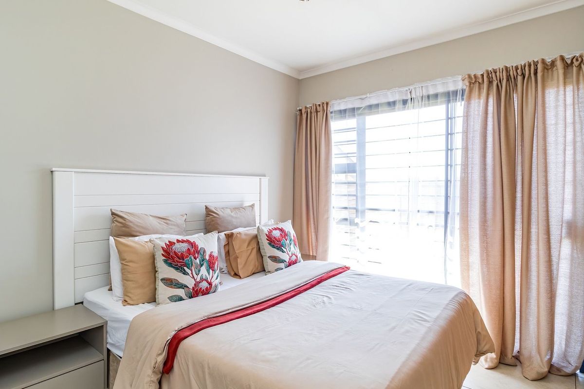 A well-lit bedroom featuring neutral wall tones, a built-in wardrobe, and a large window with natural light.