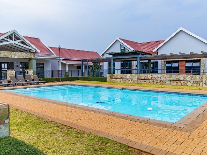 A well-maintained communal swimming pool area featuring stone-clad retaining walls, a paved deck, and a pergola, set within a townhouse complex.