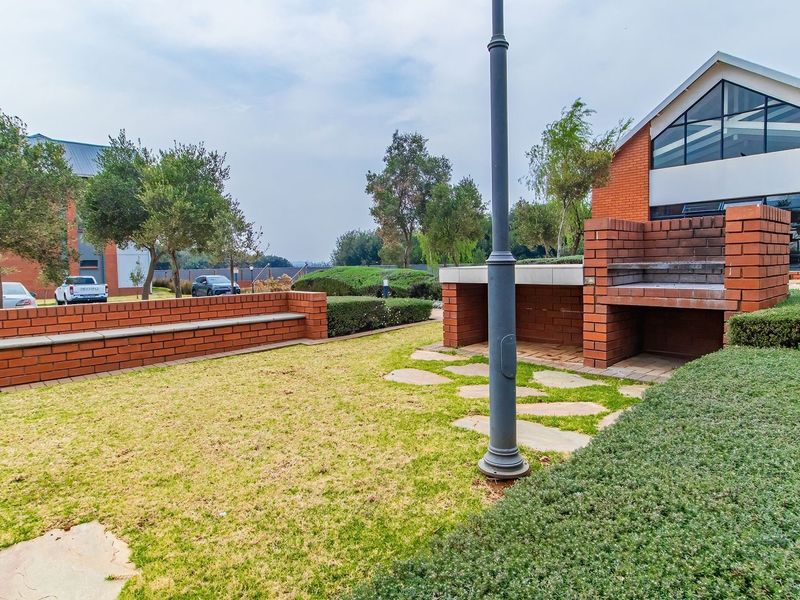 A well-maintained outdoor communal area featuring a built-in brick braai, paved pathways, and landscaped garden beds.