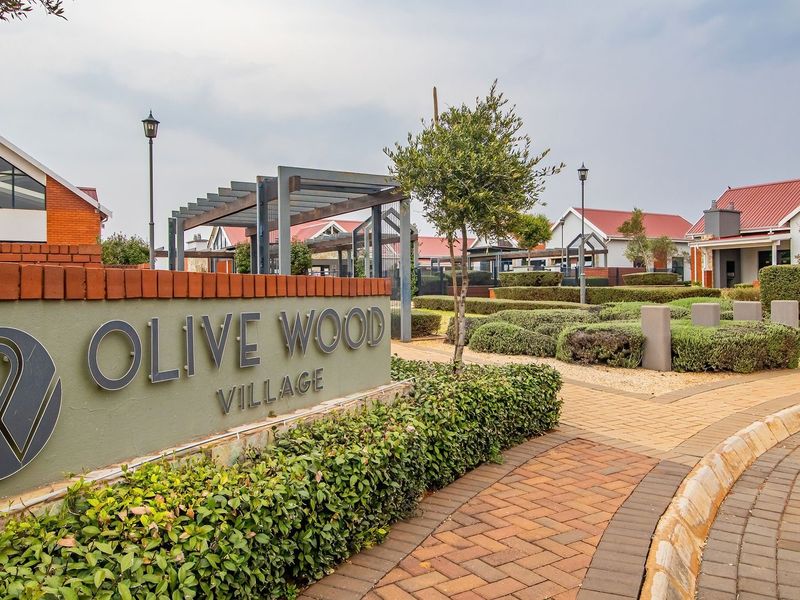 Entrance view of Olive Wood Village featuring well-maintained brick paving, landscaped gardens, and modern architectural signage.