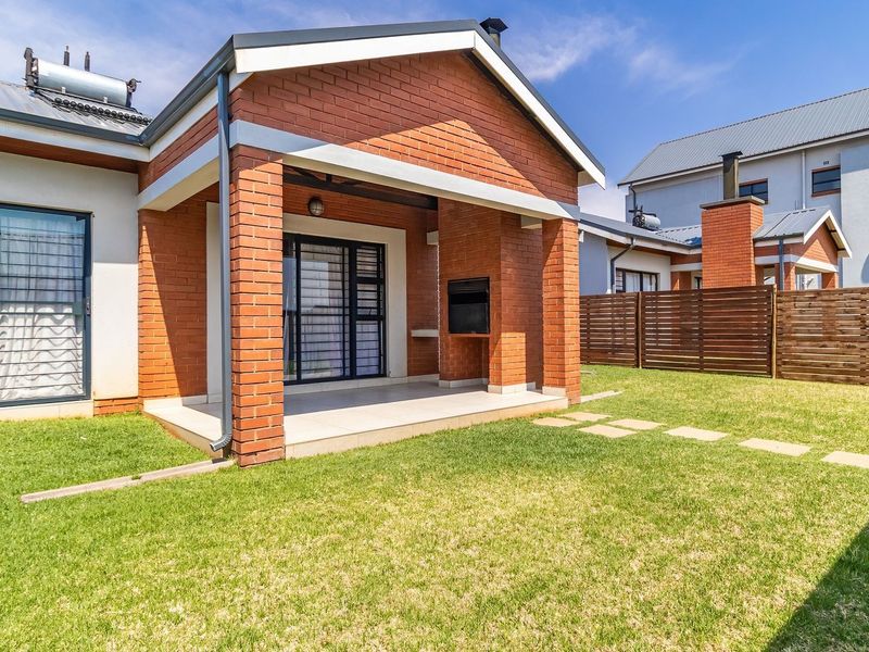 Rear view of the townhouse featuring a covered patio with a built-in braai, private garden, and solar water heating system.