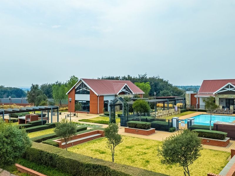 Aerial view of a well-maintained townhouse complex clubhouse featuring a swimming pool, landscaped gardens, paved walkways, and communal outdoor entertainment areas.