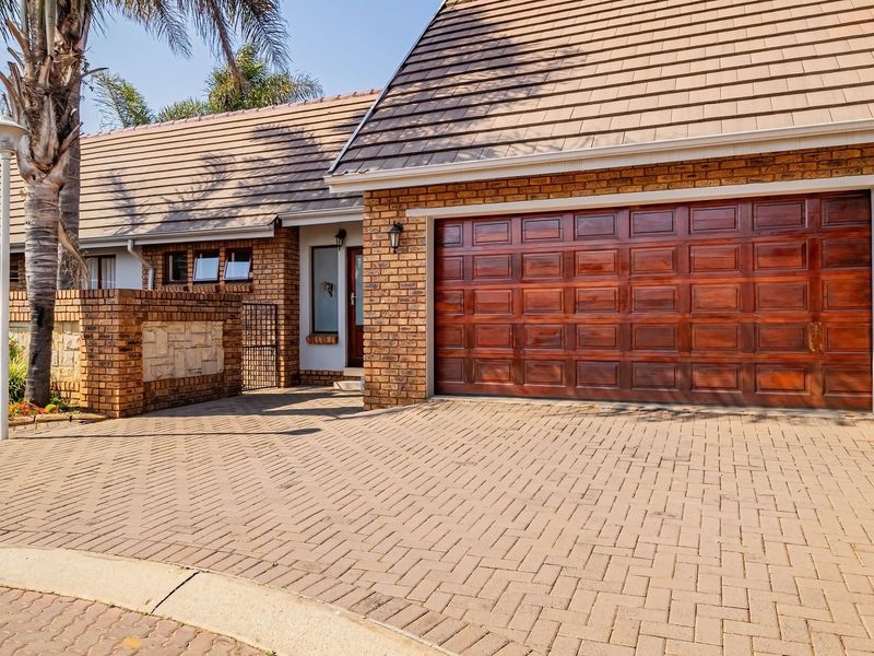 Front elevation of a townhouse featuring a brick facade, tiled roof, paved driveway, and a double garage door.