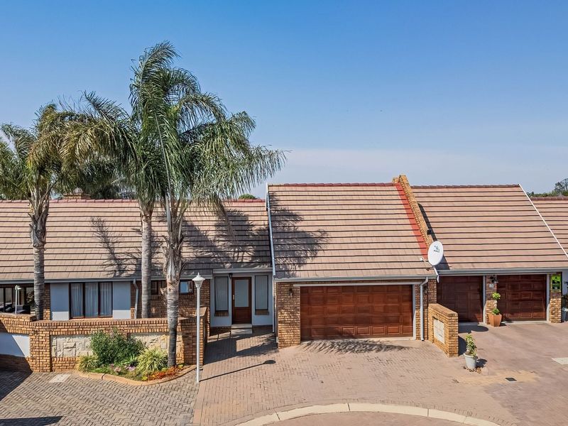 Aerial view of a townhouse complex featuring brick facades, tiled roofs, paved driveways, and multiple garage access points.