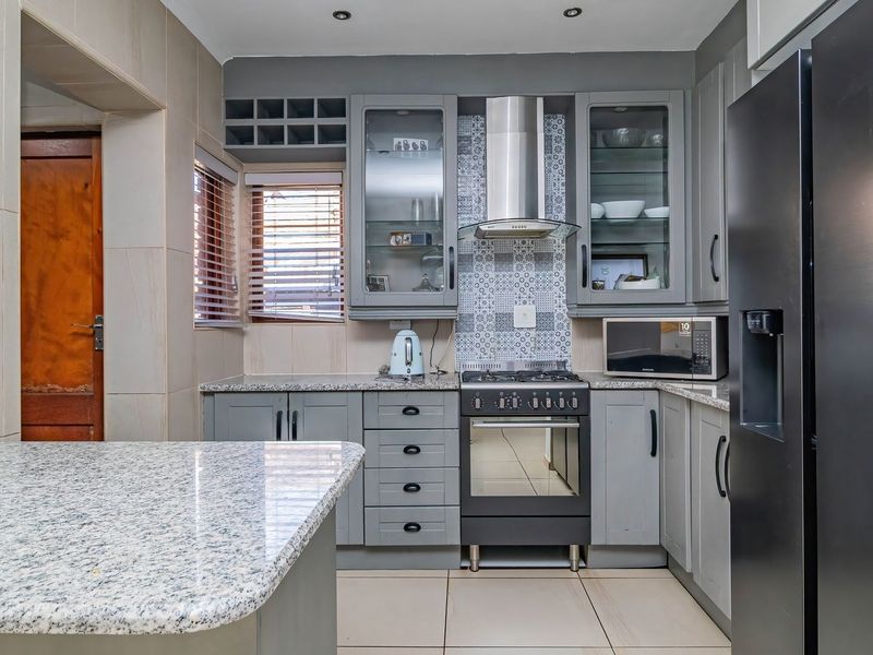 Modern kitchen featuring grey cabinetry, granite countertops, a gas stove with extractor fan, and a decorative tiled backsplash.