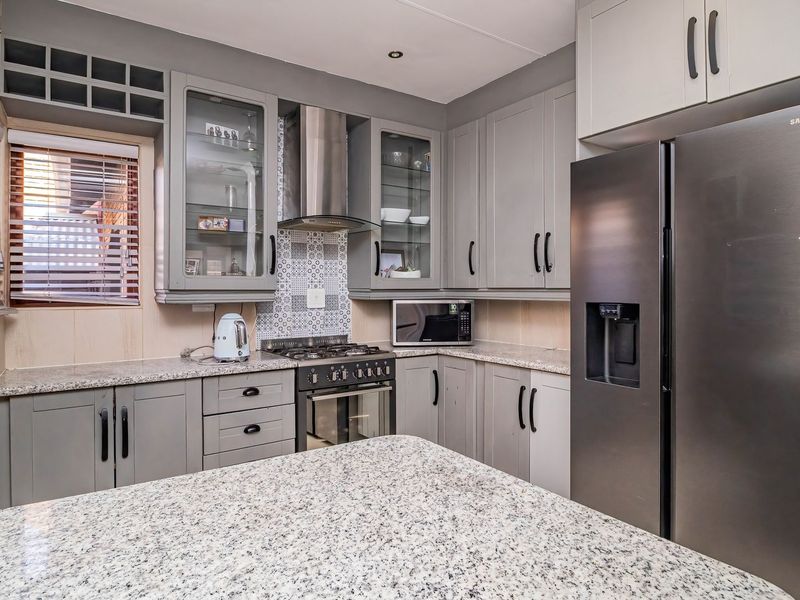 Modern kitchen featuring grey cabinetry, granite countertops, a gas hob with extractor fan, and a tiled backsplash.