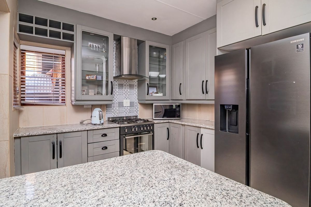 Modern kitchen featuring grey cabinetry, granite countertops, a gas hob with extractor fan, and a tiled backsplash.