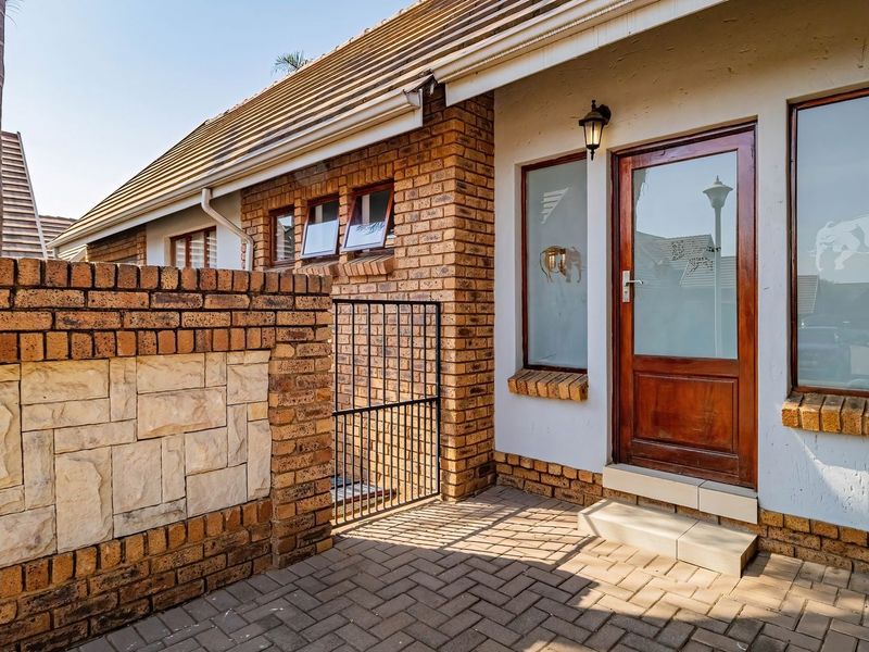 Front entrance of the townhouse featuring a brick facade, stone cladding detail, paved walkway, and a secure timber door with side windows.