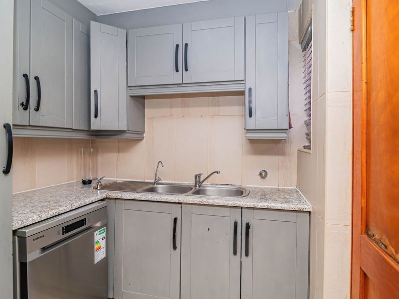 A functional scullery area featuring grey cabinetry, granite countertops, a double stainless steel sink, and an integrated dishwasher.