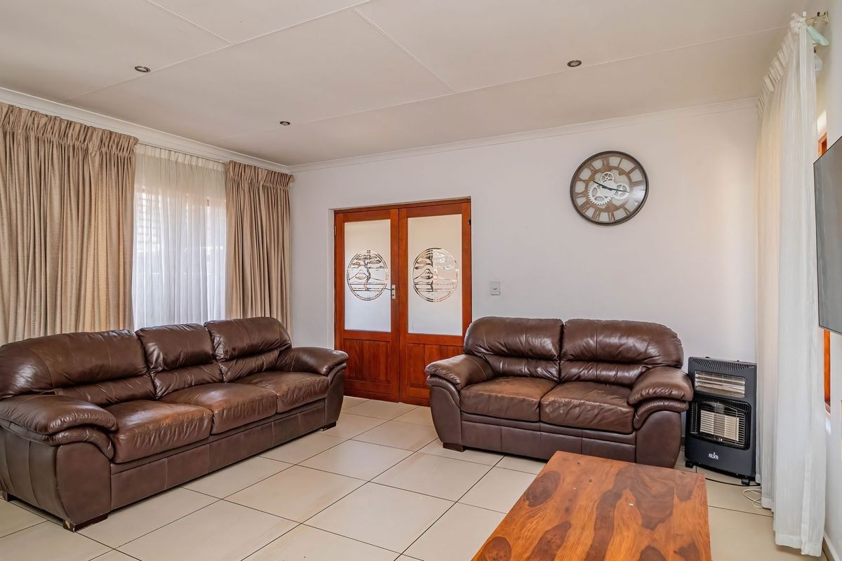 A well-lit living room featuring neutral tiled flooring, recessed ceiling lighting, and double wooden doors with decorative glass panels.