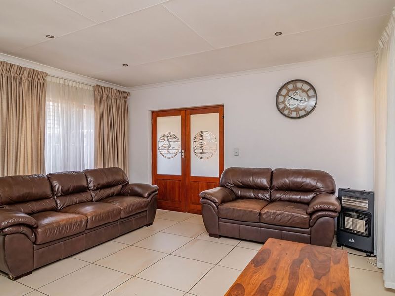A well-lit living room featuring neutral tiled flooring, recessed ceiling lighting, and double wooden doors with decorative glass panels.