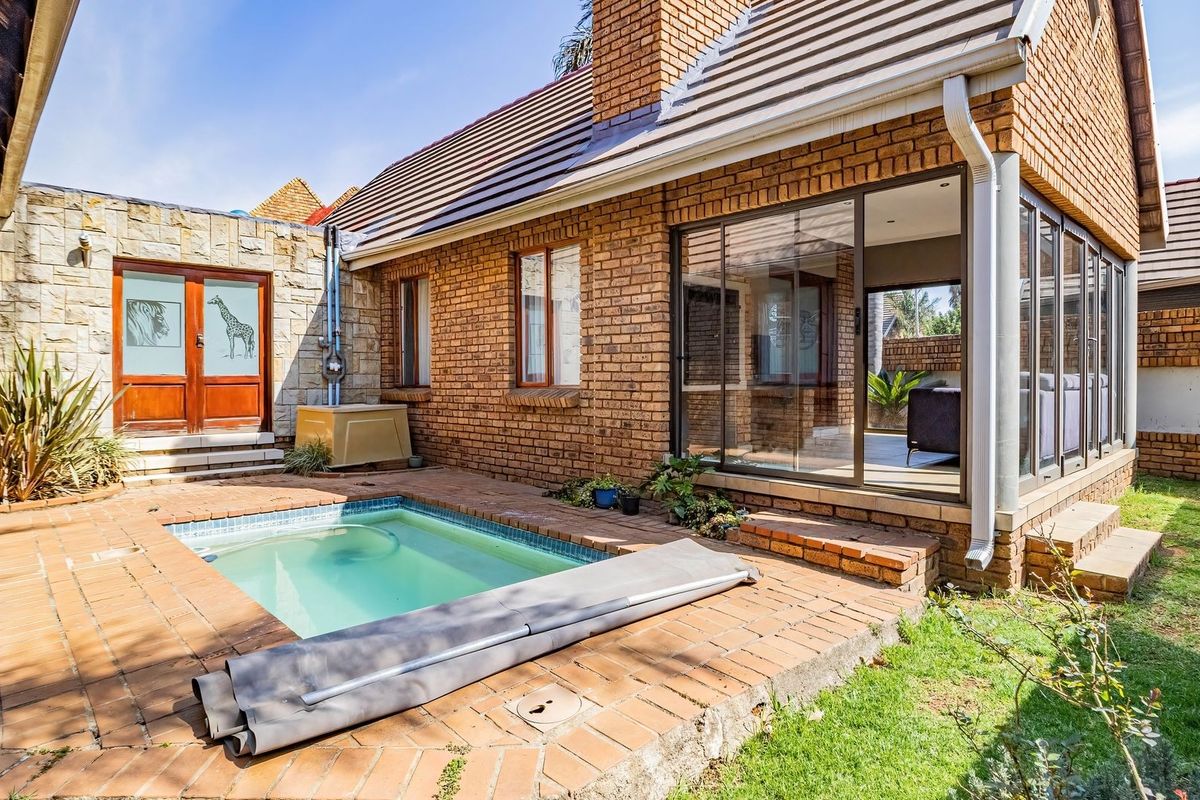 Rear exterior view of a townhouse featuring a brick facade, a private swimming pool, and a paved patio area with sliding glass door access.