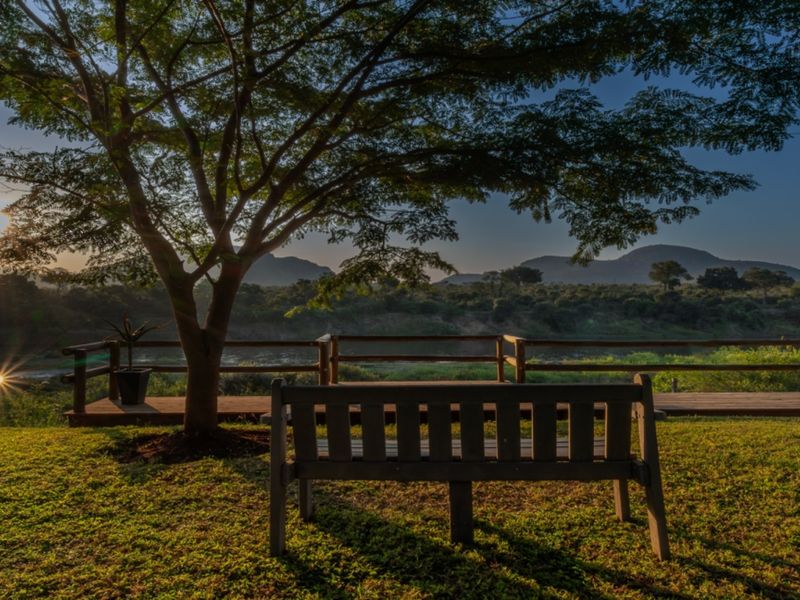 Scenic outdoor view featuring a wooden deck with timber railing overlooking a natural landscape at sunset.
