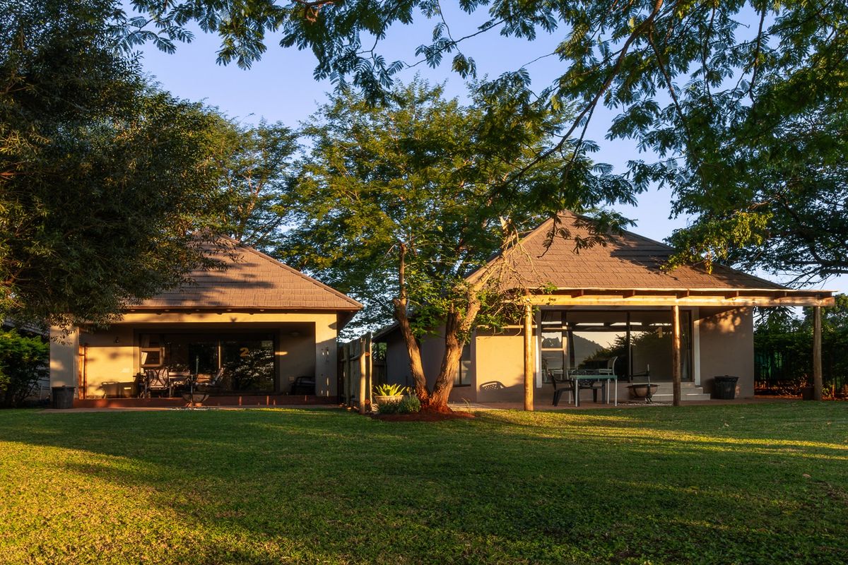 Rear view of the lodge featuring a spacious lawn, covered patio areas with wooden supports, and large sliding glass doors leading into the units.