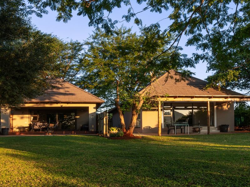 Rear view of the lodge featuring a spacious lawn, covered patio areas with wooden supports, and large sliding glass doors leading into the units.