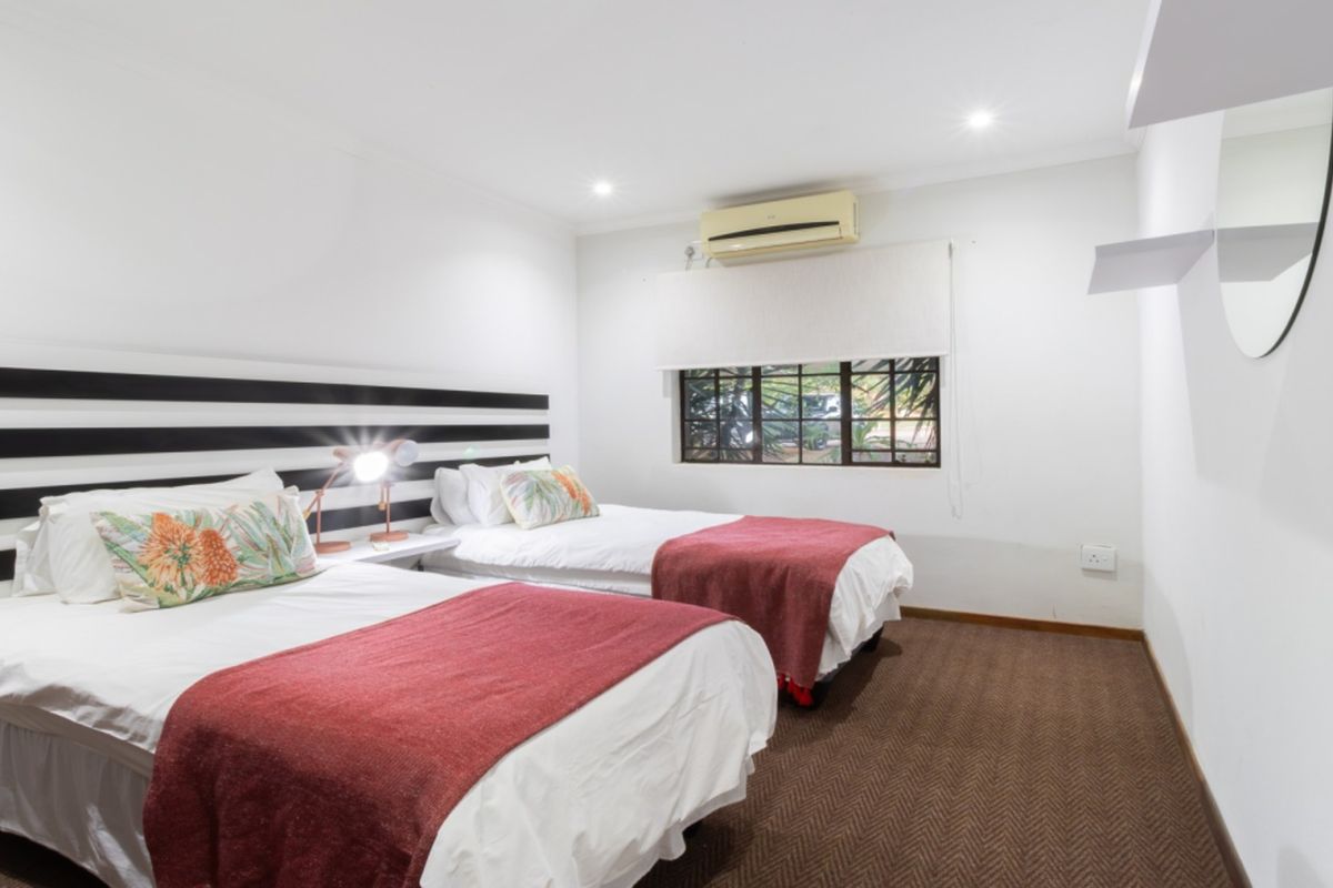 A well-maintained bedroom featuring twin beds, carpeted flooring, recessed lighting, and a wall-mounted air conditioning unit.