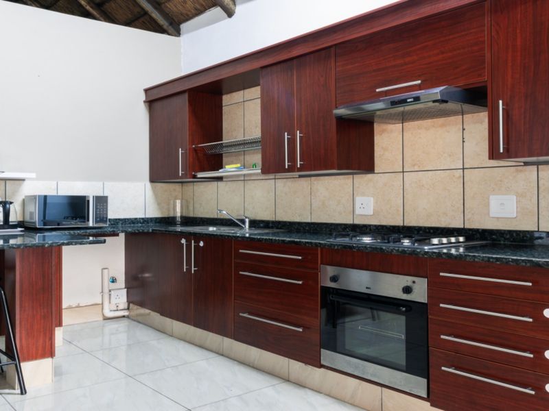 A functional kitchen featuring dark wood cabinetry, granite countertops, built-in oven, gas hob, and tiled finishes, offering a clean and practical workspace.