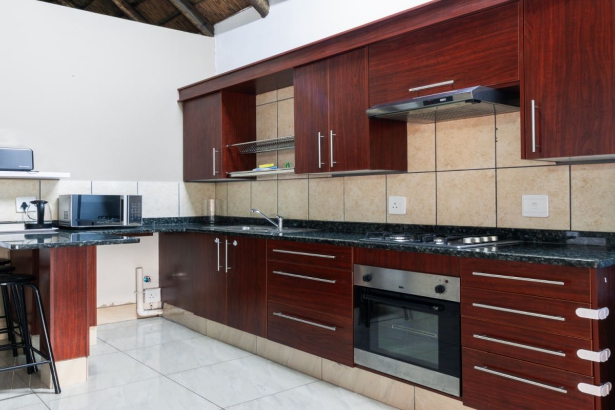 A functional kitchen featuring dark wood cabinetry, granite countertops, built-in oven, gas hob, and tiled finishes, offering a clean and practical workspace.