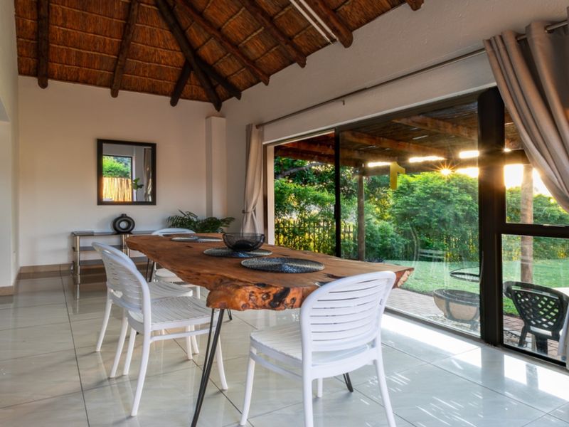 Dining area featuring a high thatched roof with exposed timber rafters, tiled flooring, and large sliding glass doors opening to the garden.