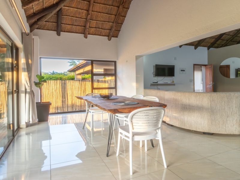 Spacious open-plan living and dining area featuring high vaulted thatched ceilings with exposed timber rafters, tiled floors, and large sliding doors leading outdoors.
