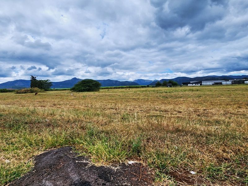 A wide-angle view of a vacant commercial land plot featuring expansive open space and scenic mountain views in the background.
