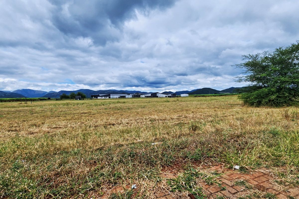 A wide-angle view of an expansive vacant commercial land plot featuring natural grass terrain and a scenic mountain backdrop.