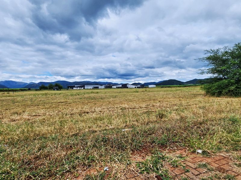A wide-angle view of an expansive vacant commercial land plot featuring natural grass terrain and a scenic mountain backdrop.