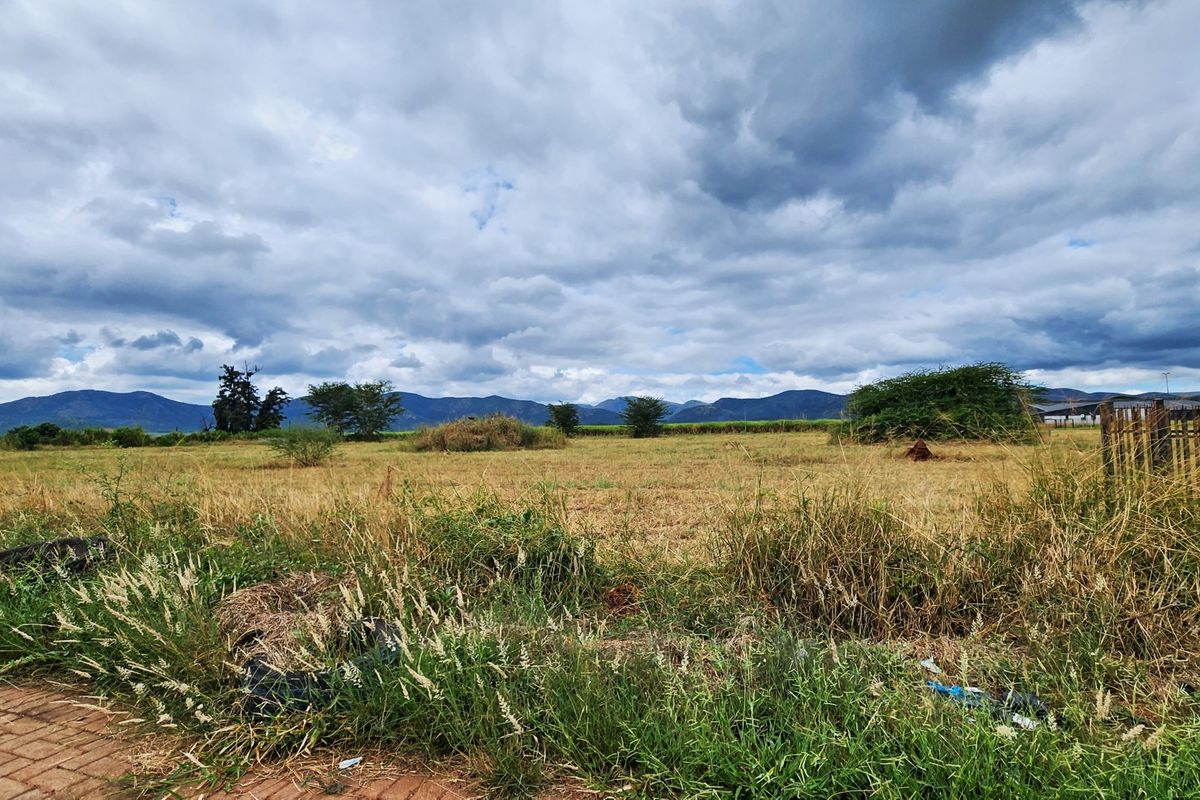 A wide-angle view of an open, undeveloped commercial land plot featuring scenic mountain vistas in the background.