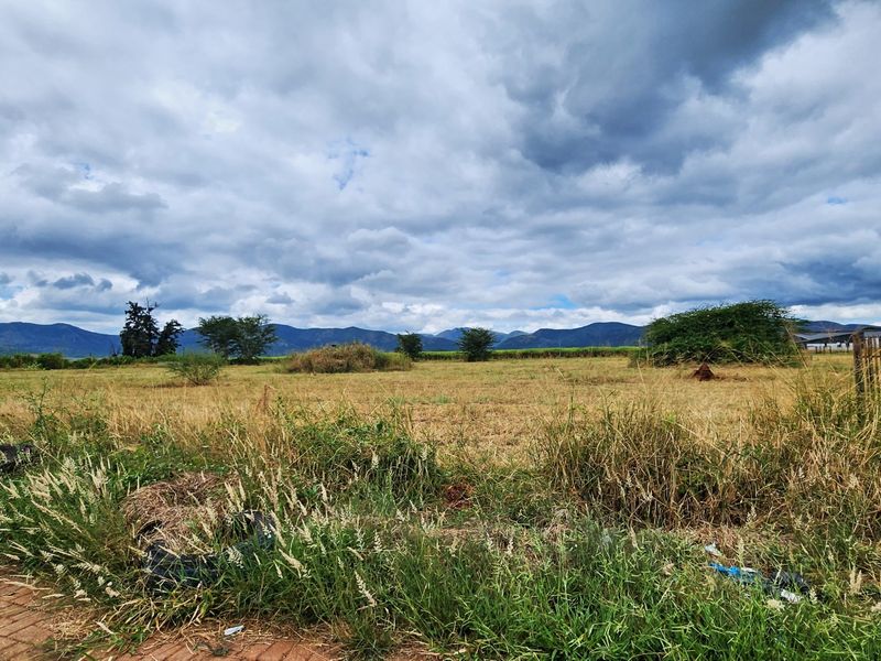 A wide-angle view of an open, undeveloped commercial land plot featuring scenic mountain vistas in the background.