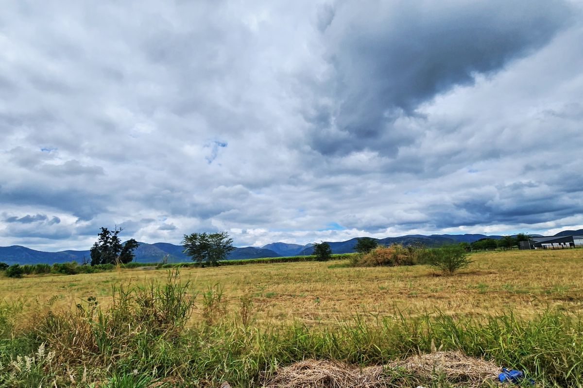 A wide-angle view of open vacant land with a scenic mountain backdrop under a cloudy sky.