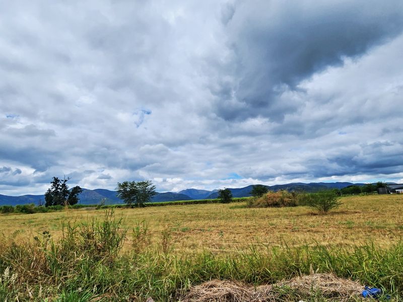 A wide-angle view of open vacant land with a scenic mountain backdrop under a cloudy sky.