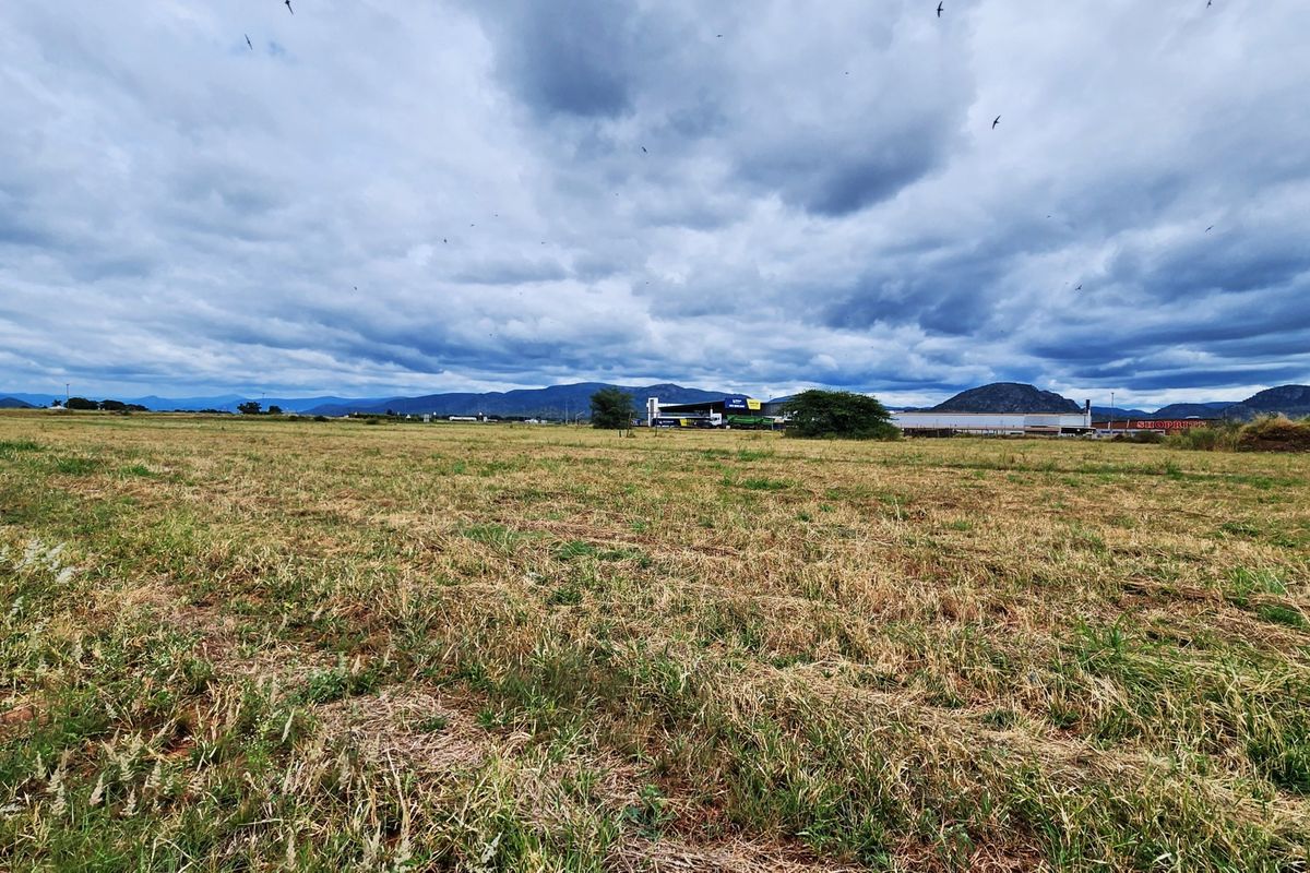 A wide-angle view of a large, undeveloped commercial land plot featuring dry grass and distant mountain views.