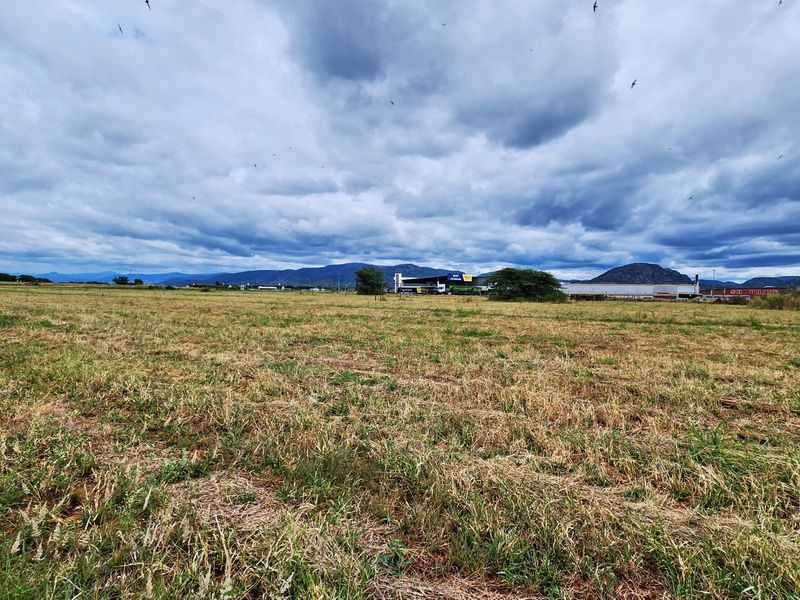 A wide-angle view of a large, undeveloped commercial land plot featuring dry grass and distant mountain views.
